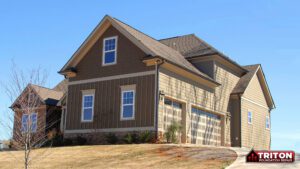 A two-story suburban home with beige and brown siding, a steeply pitched roof, and a three-car garage with glass-paneled doors